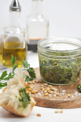 Green pesto sauce in a jar, large salt, garlic clove, pine nuts on a wooden plate. In the frame,...