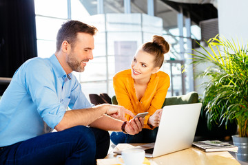 Two business partners smiling talking about work with smartphone and laptop