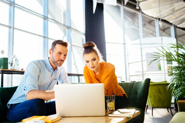 Two serious coworkers looking at laptop during business meeting in cafe