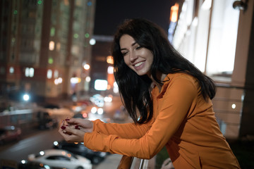 Smiling woman standing on the terrace, night city background