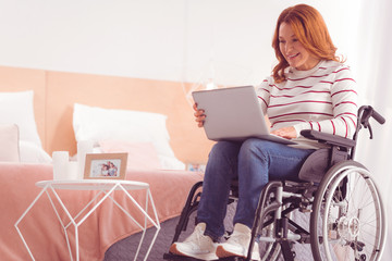Active user. Cheerful nice paralyzed woman using laptop while resting at home
