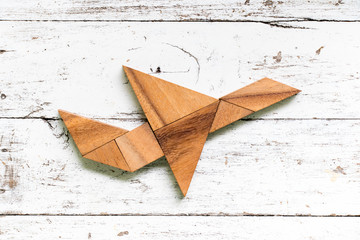 Tangram puzzle in flying airplane shape on old white wood background