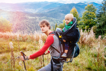 The man traveler with the child. Father carries her son in a backpack. Male took the child to the mountains. Traveling with children. A man is walking with his toddler. Sun glare effect.