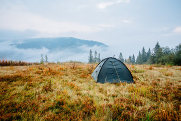 Morning in mountains in autumn time. Camping tent on the grass at meadow with beautiful landscape view.