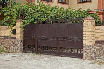 old brown iron gate and a brick fence in green vegetation on the street