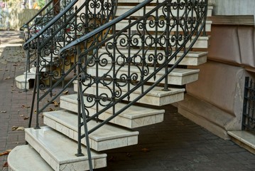 Staircase with gray concrete steps and iron black handrails with a forged pattern near the wall on...