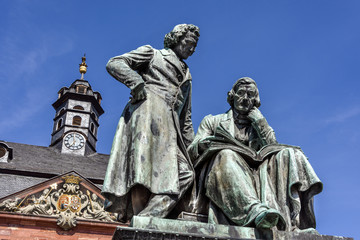 Fototapeta na wymiar Germany, Hanau: National memorial statue of famous Grimm Brothers in the city center of the German town with town hall and blue sky in background - concept culture fairy tales art travel history