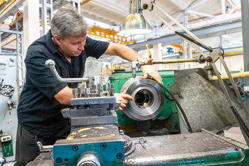 A worker, a man in a black shirt and safety glasses, checks the part for suitability for use in...