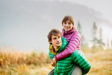 Travel, tourism and people concept.Lovely couple, camping, mountains, nice forest view. Guy are piggybacking his girlfriend so happy, smiling. Autumn nature active lifestyle.
