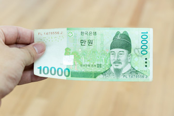 Business man hold south korea banknote 10000 korean won on wood background