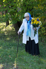 grandmother with a cane and flowers on the background of trees