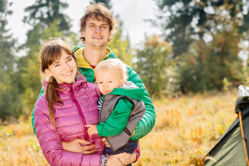 Fototapeta na wymiar Portrait of happy family mother, father and toddler son wearing colorful duck jacket are traveling on Carpathain mountains. Traveling with children, tourism and people concept. Copy space.