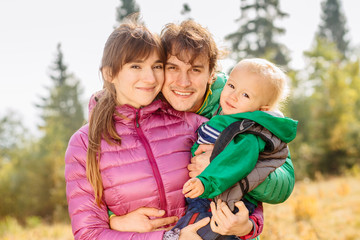 Portrait of happy family mother, father and toddler son wearing colorful duck jacket are traveling on Carpathain mountains. Traveling with children, tourism and people concept. Copy space.