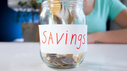 Closeup image of coins falling in glass jar labeled Savings