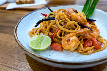 Spaghetti tom yum mun goong with on white plate wooden table.