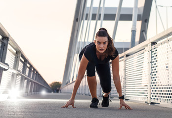 Female runner running outdoor on bridge. Young woman is at start position.