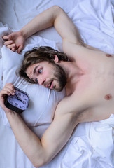 Man bearded unshaven handsome guy lay on pillow near alarm clock top view. Toughest part of morning simply getting out of bed. Guy relaxing bed before alarm clock ringing. Get up early morning tips