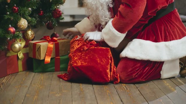 Santa Claus laying out presents under christmas tree