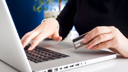 Closeup photo of young woman using laptop and holding credit card