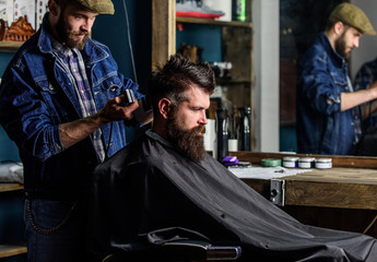 Barber with clipper trimming hair on nape of client. Hipster client getting haircut. Hipster lifestyle concept. Barber with hair clipper works on haircut of bearded guy barbershop background