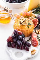 Cheese plate served with grapes, jam, figs, crackers and nuts on a white background. Copy space.