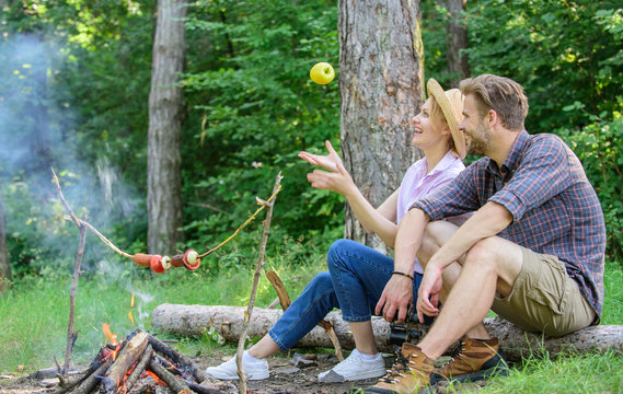 Idyllic picnic date. Pleasant smell of roasted food makes picnic atmosphere perfect. Picnic roasting food over fire. Couple in love relaxing sit on log having snacks. Family enjoy weekend in nature