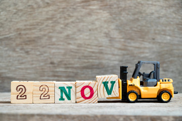 Toy forklift hold block V to complete word 22nov on wood background (Concept for calendar date 22...