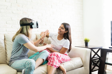 Woman Looking At Friend Wearing Virtual Reality Headset At Home