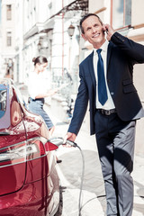 Ecological petrol. Cheerful male person keeping smile on his face and looking aside while fuelling his car