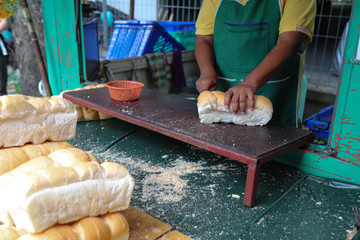 Closeup of long loafs cutting by female seller for selling to people for fish feeding in public park.