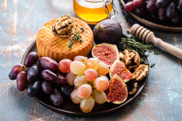 Cheese plate served with grapes, jam, figs, honey and nuts on a rustic background. Copy space.
