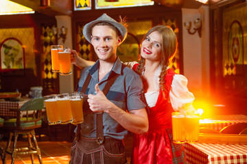 Cheerful man and girl waiters in national costumes at the celebration octoberfest hold in their hands a lot of beer mugs.