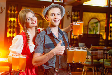 Cheerful man and girl waiters in national costumes at the celebration octoberfest hold in their hands a lot of beer mugs.