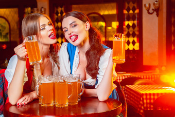 Young girls in national costumes with glasses of beer in their hands show their tongue at the Oktoberfest festival.