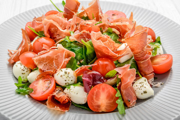 Salad with fresh vegetables with dried tomatoes, meat and mustard, mozzarella, prosciutto