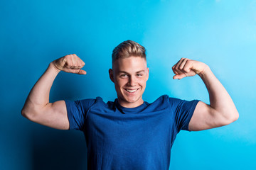Portrait of a cheerful young man in a studio, flexing muscles.