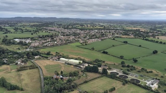 Aerial view, zoom in move. Sewage works, Tarvin residential area houses among fields on Cheshire countryside.