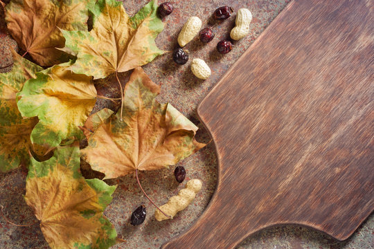 Autumn leaves, hawthorn berries, peanuts and an old wooden cutting board