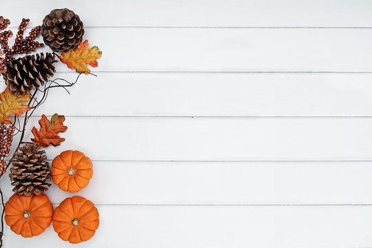 Rustic fall background of autumn leaves, pine cones and mini pumpkins with free copy space for text over a white rustic background. Image shot from overhead.