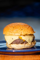 A close look on a cheese burger served and ready to eat, with tomato sauce and a drink in the background