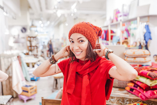 young woman trying and choosing warm hat in fashion store