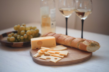 white wine,green gpapes in the plate,slaced cheese and baguette on the cutting board/ 