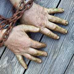 Man's hands chained with old rusty thick chain on the wooden boards