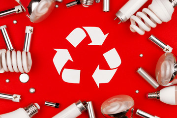 Old used metal lithium alkaline batteries cells and led, incandescent halogen cfi fluorescent, lumens light bulbs tube on red background. Reuse recycling sign symbol environment light bulbs concept.