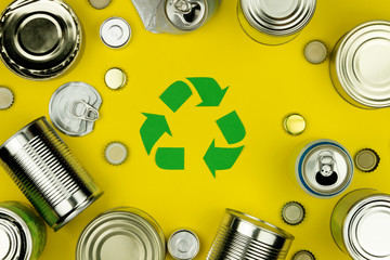 Green recycle reuse sign symbol with metal aluminium cans, covers, jars on yellow background. Eco...