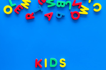 Early childhood development concept. Word kids written by plastic letters of toy alphabet on blue background top view copy space