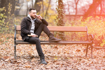 Fototapeta premium A handsome young hipster man sitting on a bench and adjusting his moustaches.