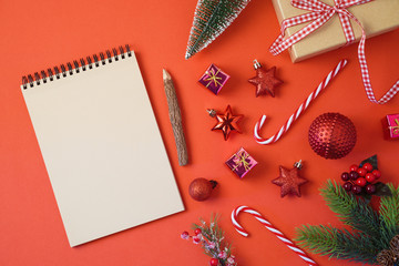 Christmas holiday background with notebook and decorations on red table. Top view from above