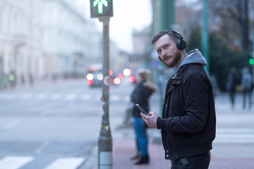 A handsome young hipster man checking his smartphone while waiting at a crosswalk.