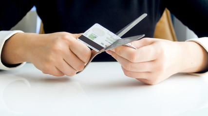Closeup image of young woman cutting credit card with scissors